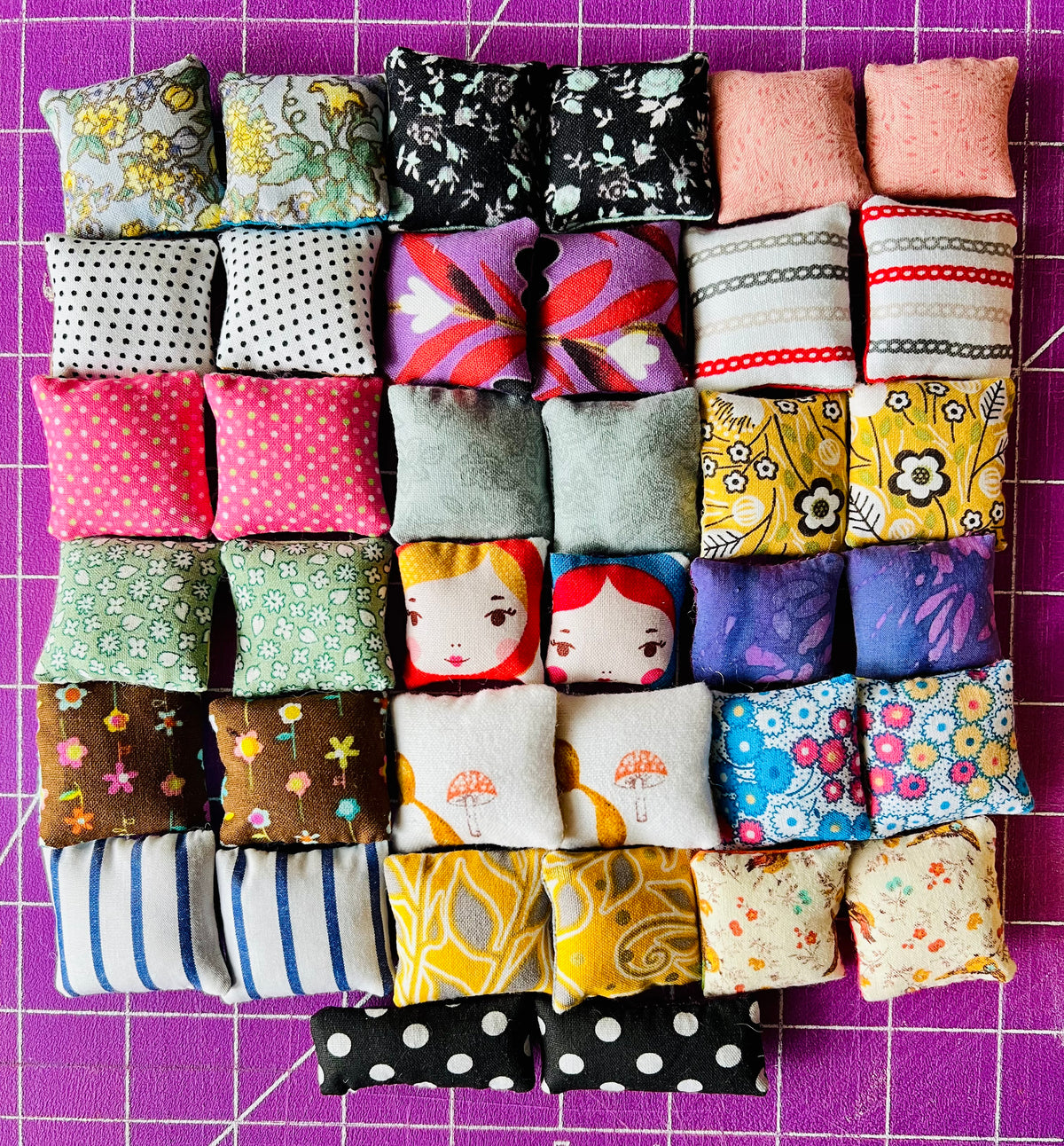 Collection of small fabric pillows in various patterns on a purple grid background