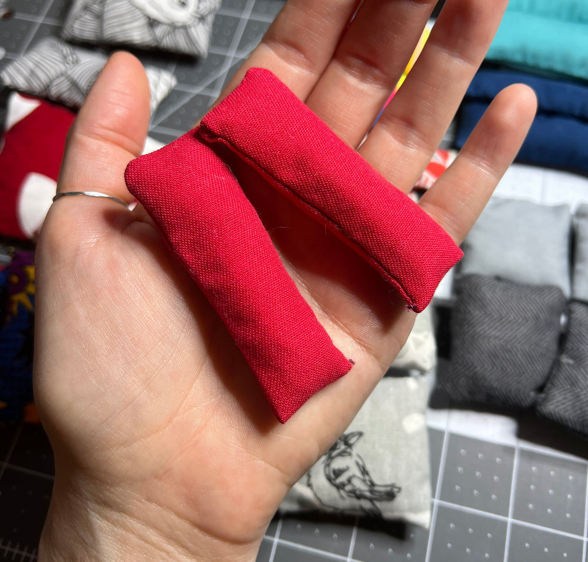 Two doll pillows, held in hand for scale, with other pillows seen in background