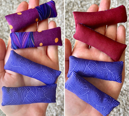 Two sets of fabric pillows held in hands, one set purple with swirl patterns and the other set has purple patchwork on one side and maroon red on the other.