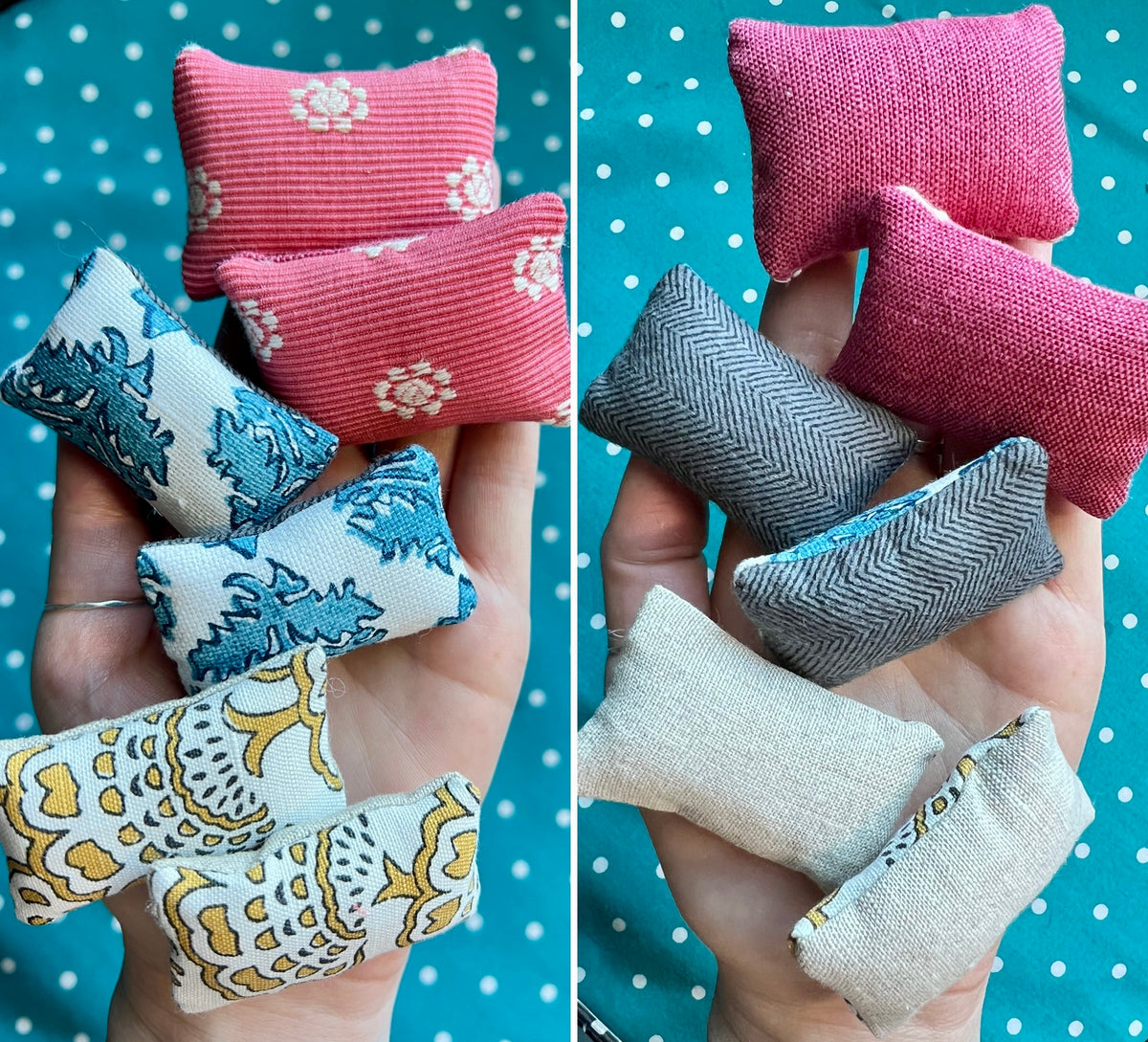 Set of small fabric pillows in various patterns held in hands against a polka dot background.