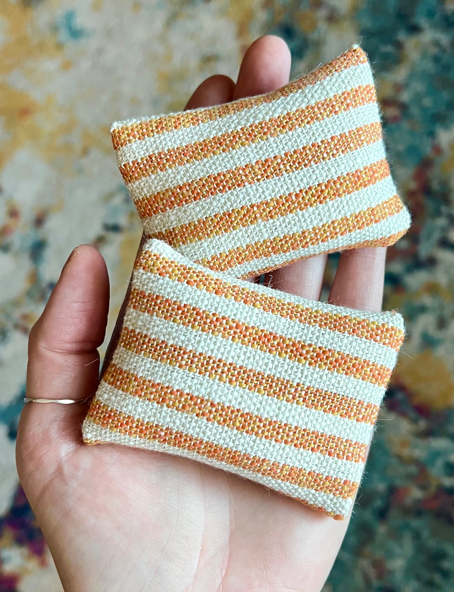 Two striped fabric pillows held in a hand against a patterned background