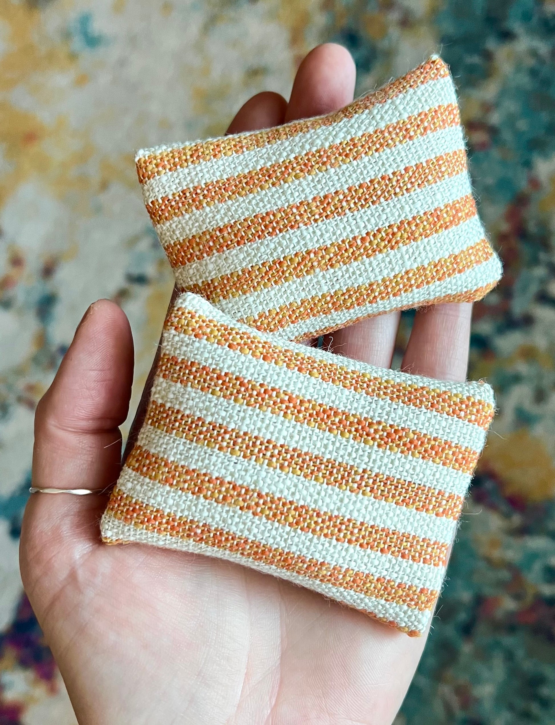 Two striped fabric pillows held in a hand against a patterned background