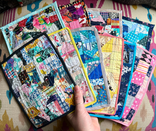 Collection of colorful doll quilts held by a hand on a patterned surface.