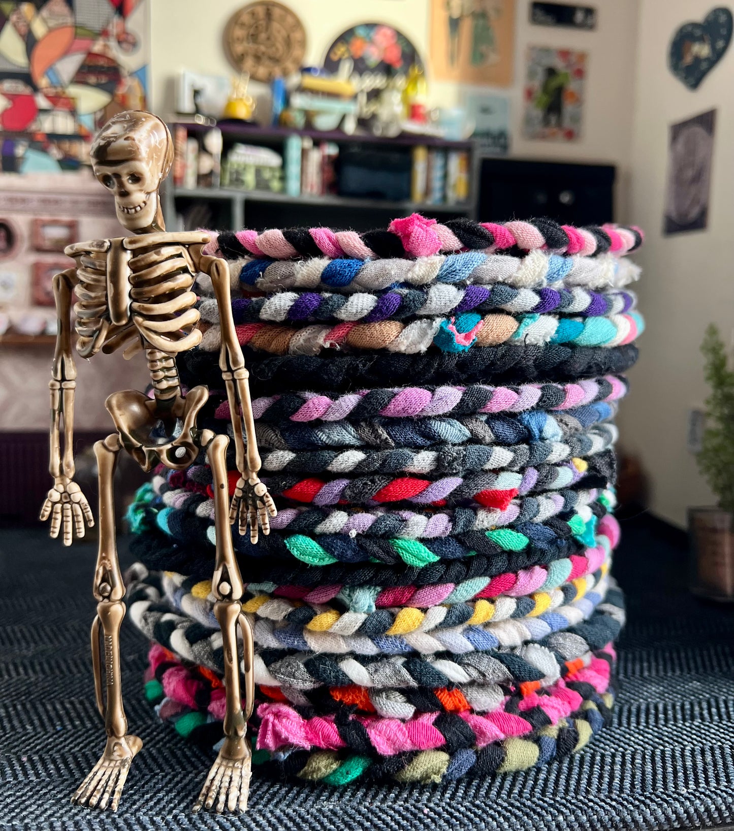 Stack of colorful braided mini rugs with a skeleton figure on top in a room setting.