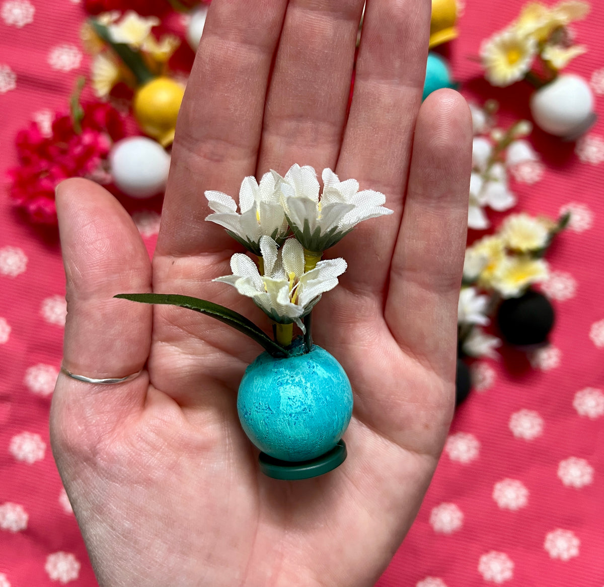 Small blue ball doll vase with white flowers held in a hand against a polka dot background