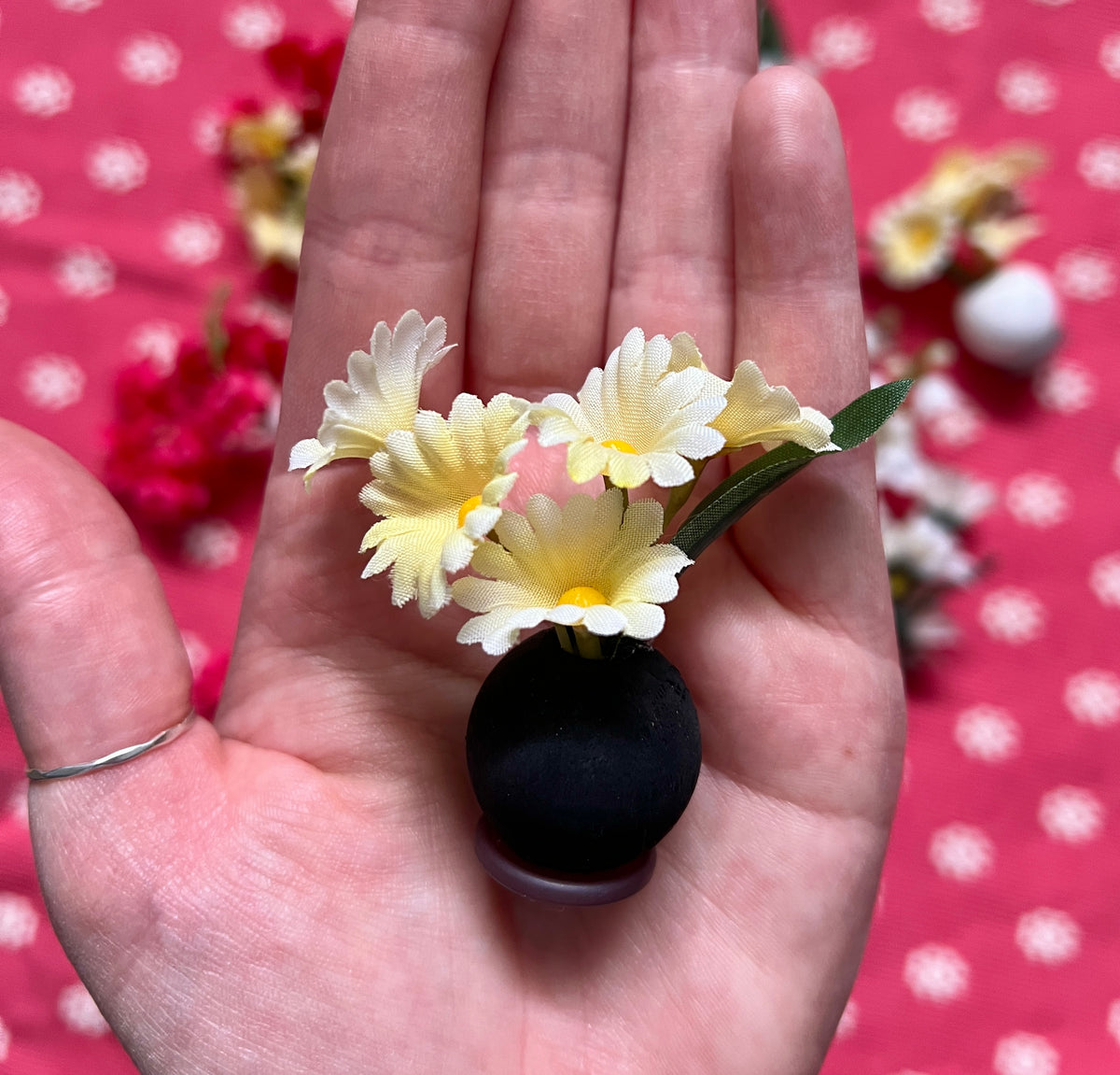 Small black bead “vase” with yellow flower clips held in a hand against a polka dot background