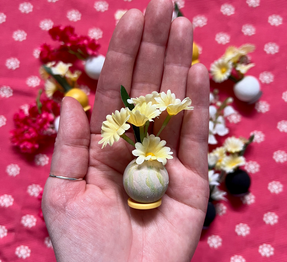 Hand holding a small decorative flower arrangement against a pink polka dot background