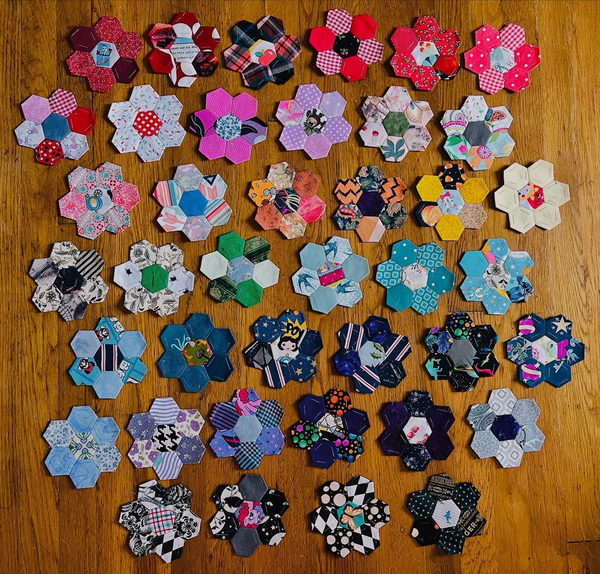 Collection of colorful fabric epp hexie flowers on a wooden surface
