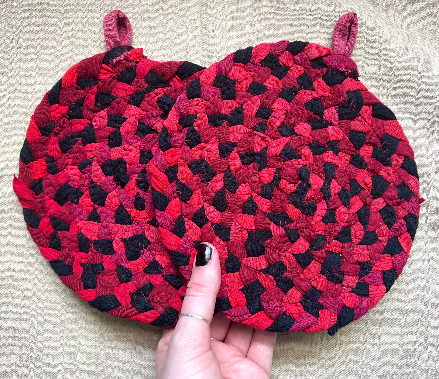The back of two trivet potholders, to show off stitching, held against a linen surface.