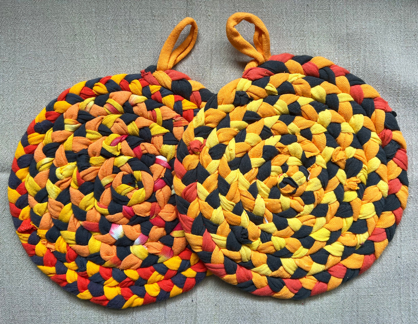 A set of two trivet potholders, side by side, lay flat on a linen surface.