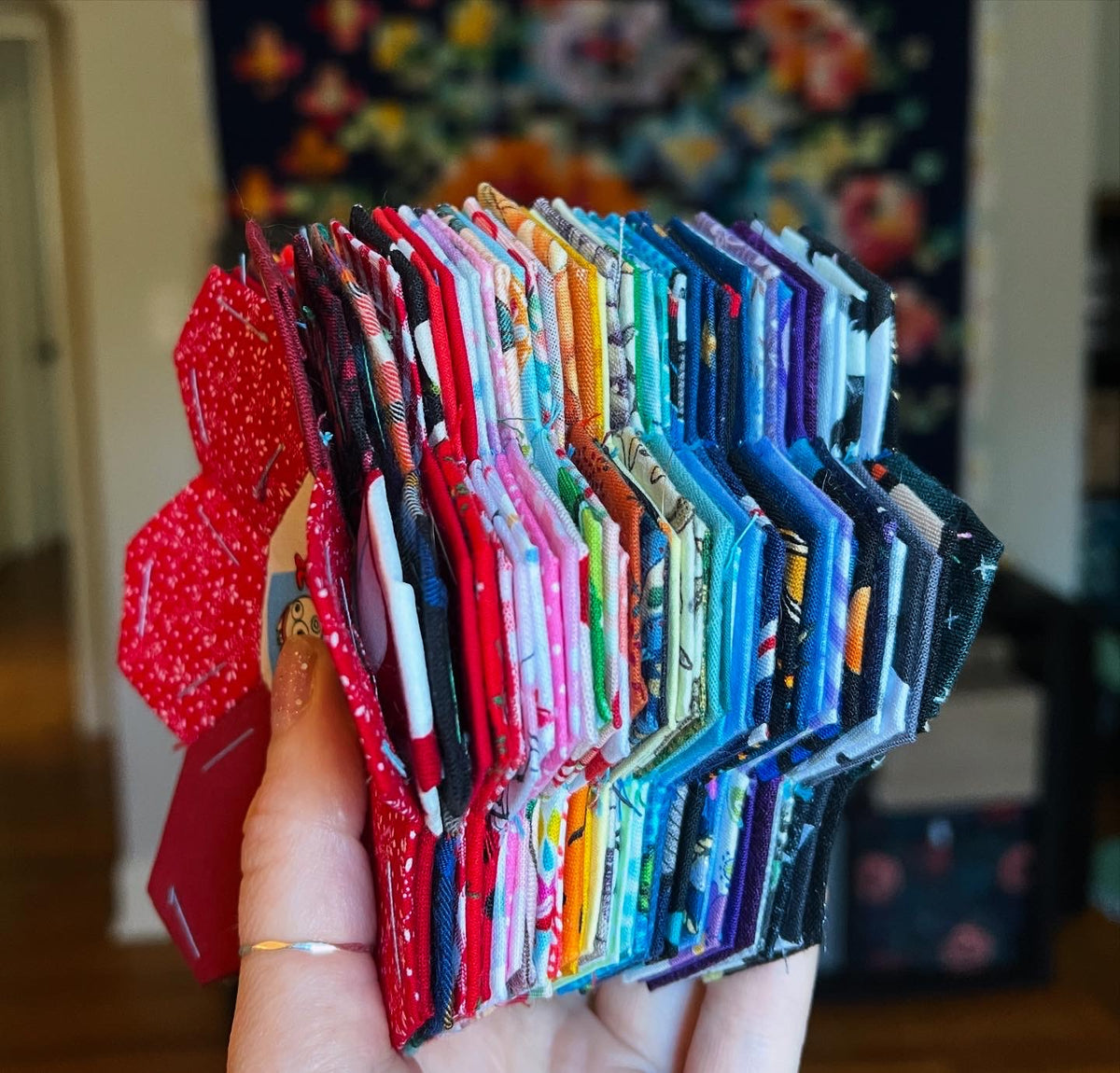 Hand holding a colorful assortment of fabric epp hexie flowers with a blurred background