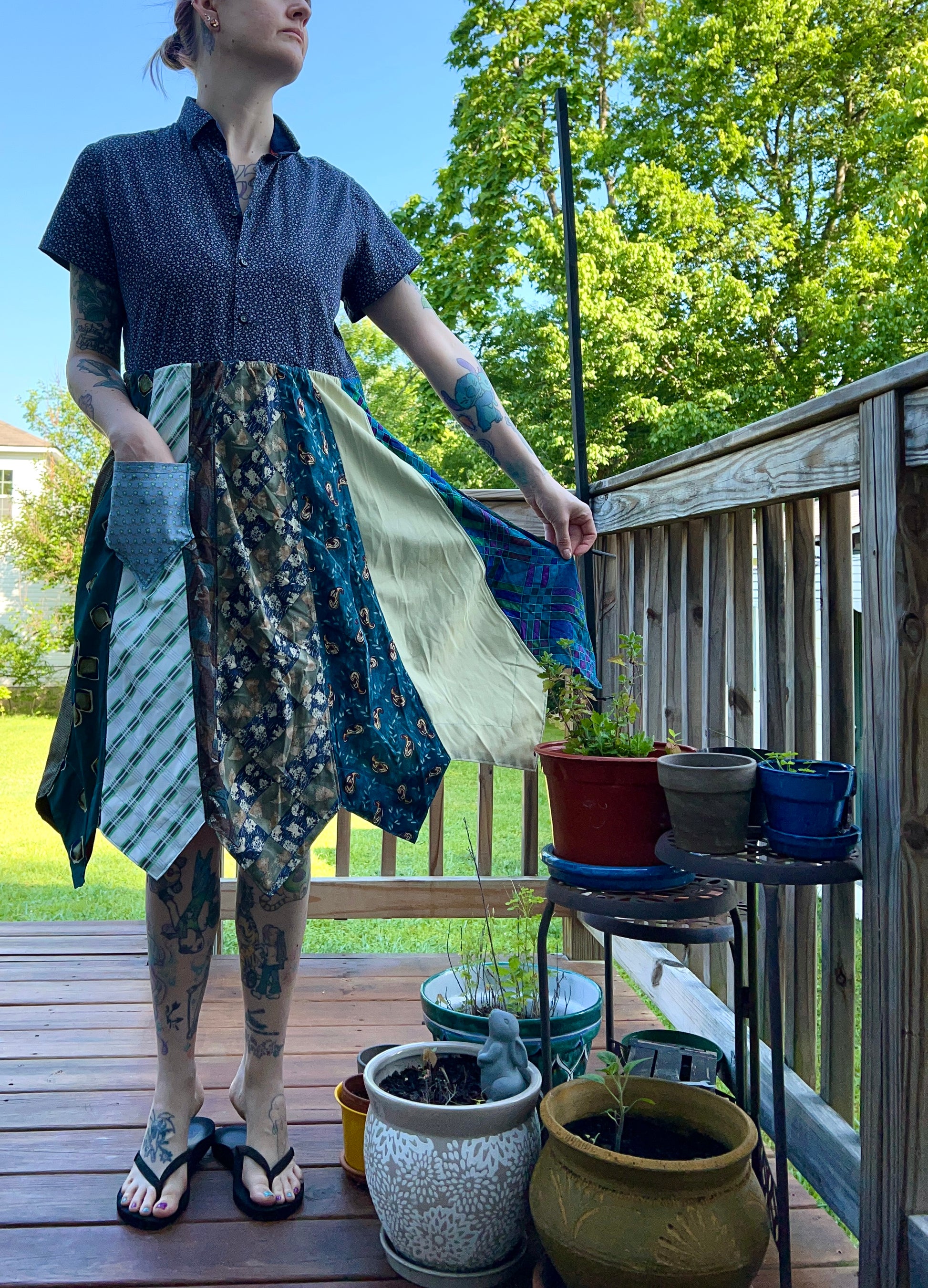 A tattooed model shows off the skirt of the necktie shirtdress, with one hand in the front pocket, and the other holding up the skirt to the side.