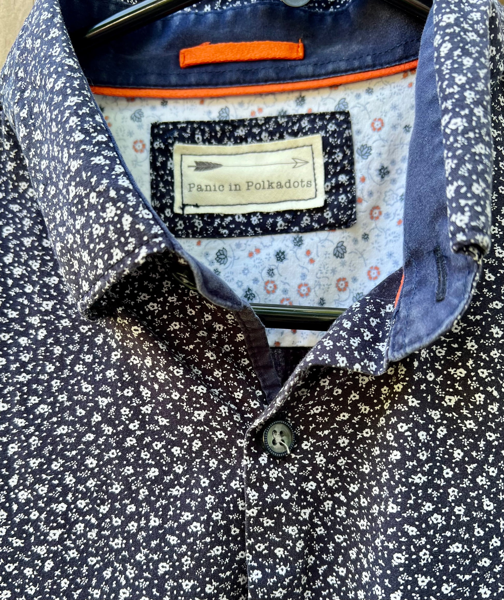 Closeup of label which has an arrow sketch, and the words "Panic in Polkadots" below, on a blue floral shirt.