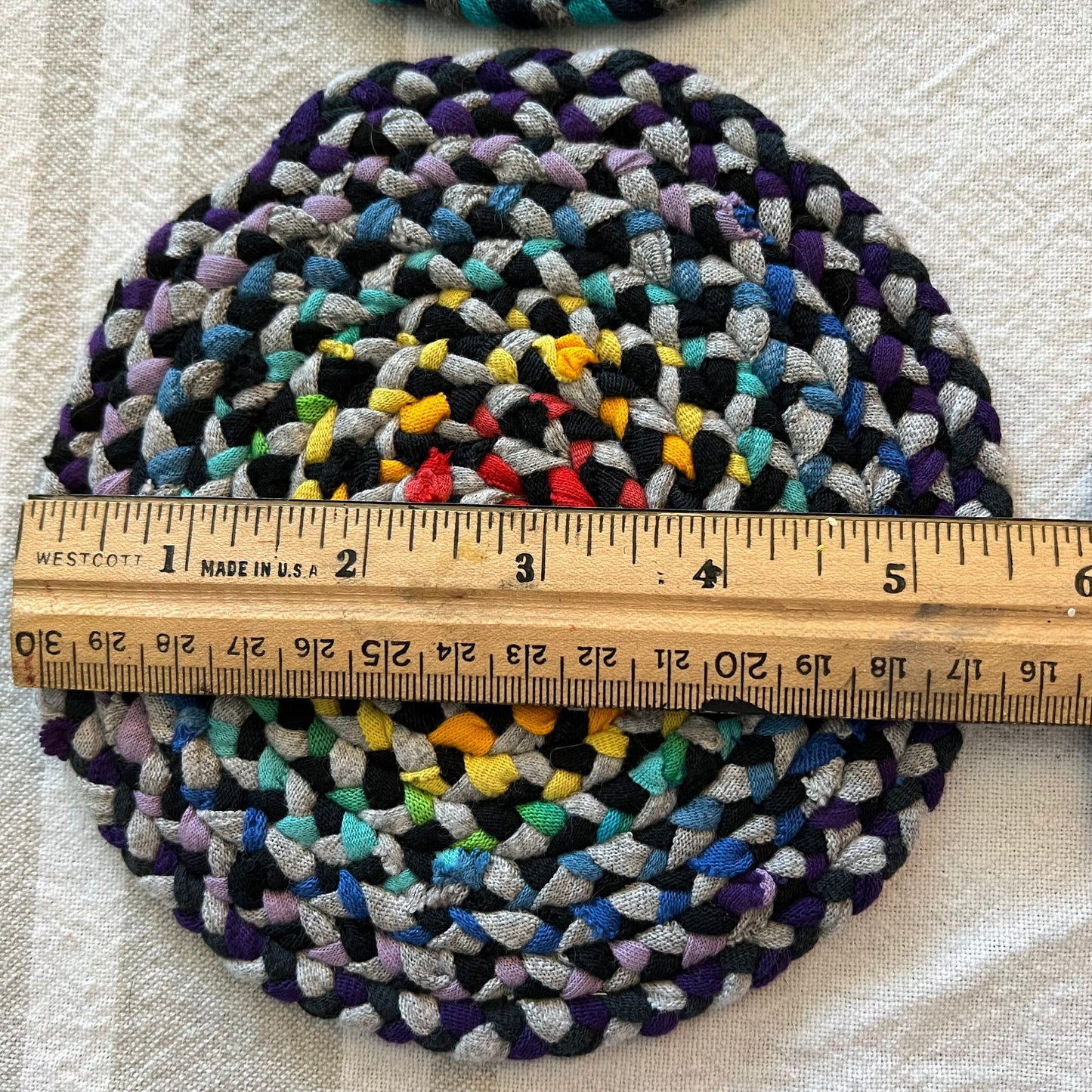 aerial view of miniature dollhouse rug, with a ruler on the top indicating a diameter of just over 5 inches.