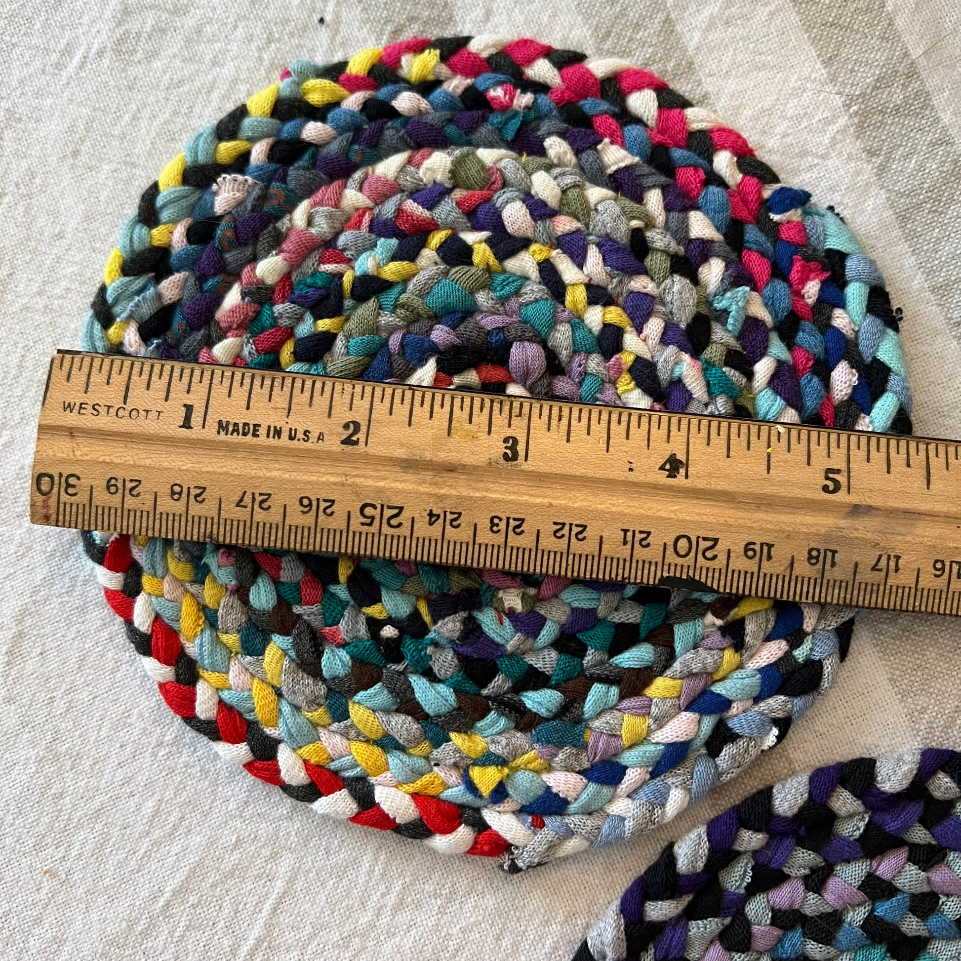 aerial view of miniature dollhouse rug, with a ruler on the top indicating a diameter of just over 5 inches.