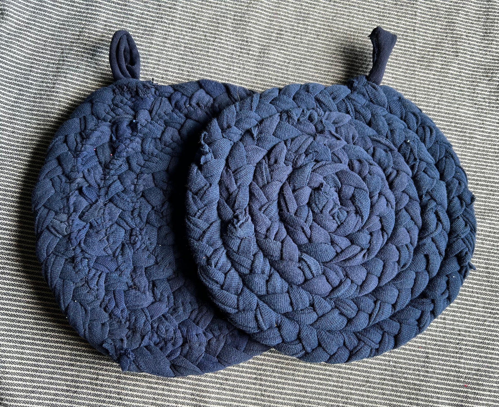 A set of two trivet potholders, side by side, lay flat on a fabric surface.