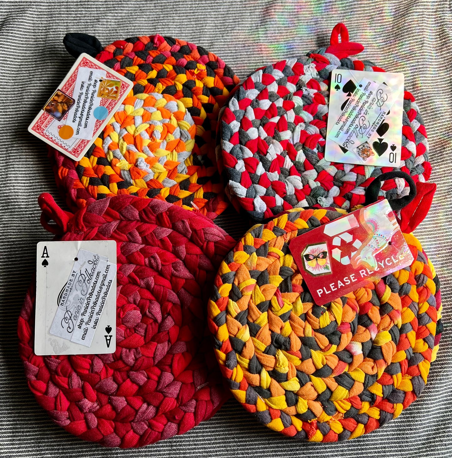 Four sets of trivet potholders, all laid together in a pile. Each set has a playing card with info about Panic in Polkadots.