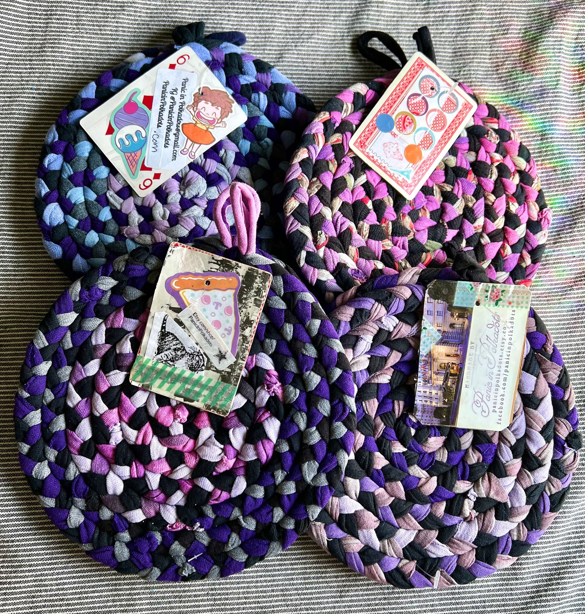 Four sets of trivet potholders, all laid together in a pile. Each set has a playing card with info about Panic in Polkadots.