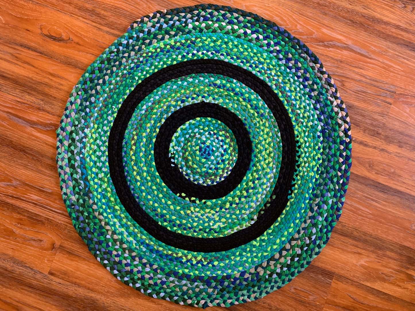 aerial view of green monet tshirt rug, with various greens sparkling throughout, and two black strips to form a bullseye