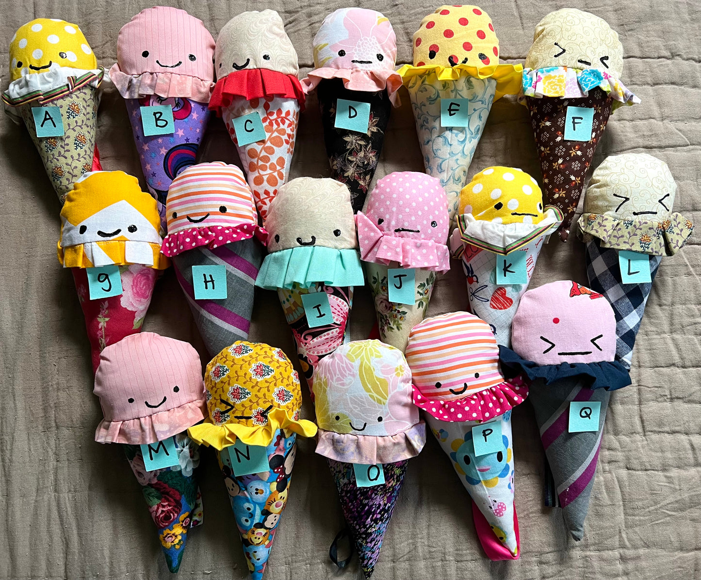 A group of colorful ice cream cone plushies, all lined up next to each other with coordinating letters on top of each one for easy selection.