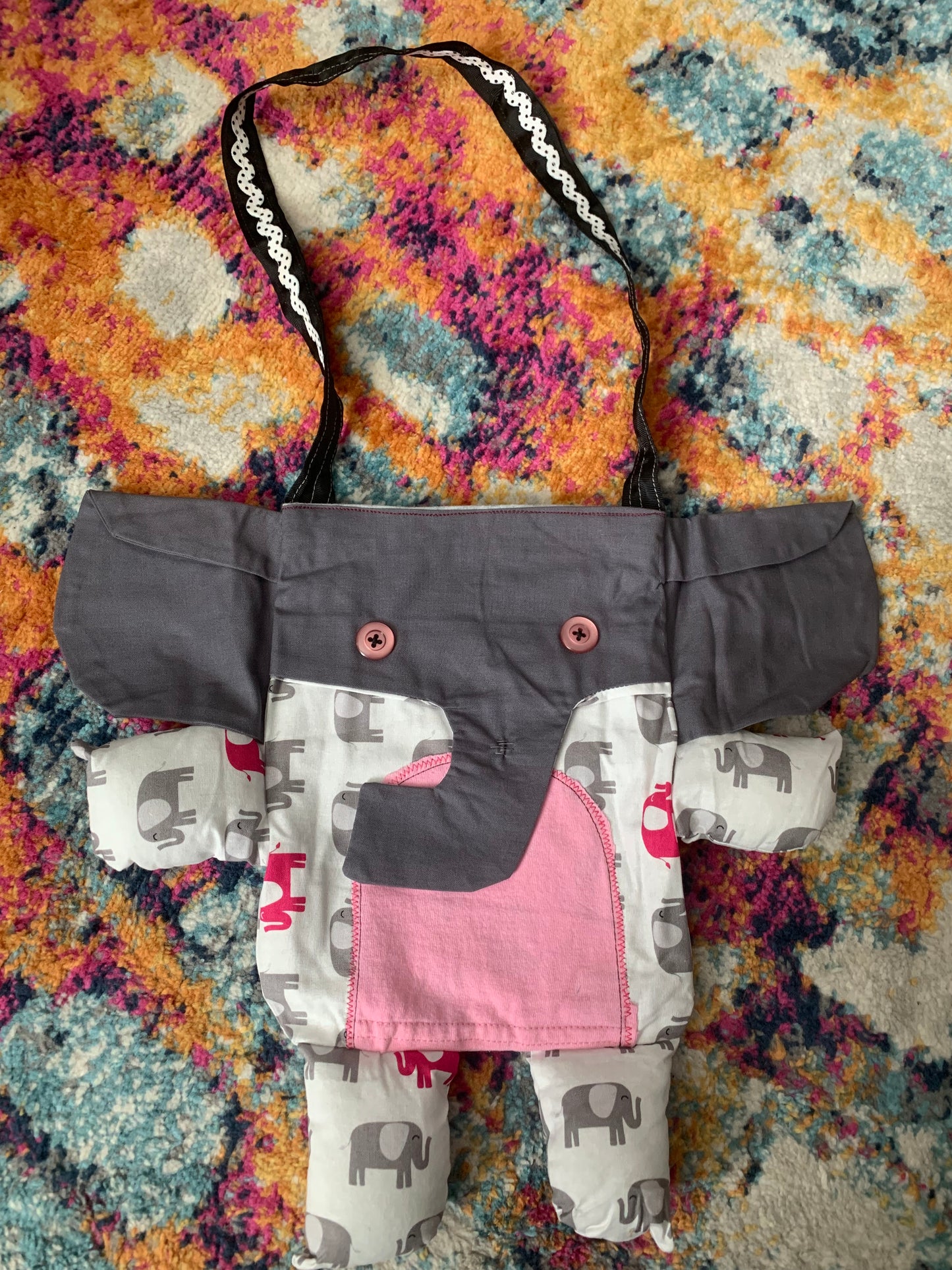 elephant tote bag, with black and white strap. Grey trunk and ears, elephant print body, with pink tummy.