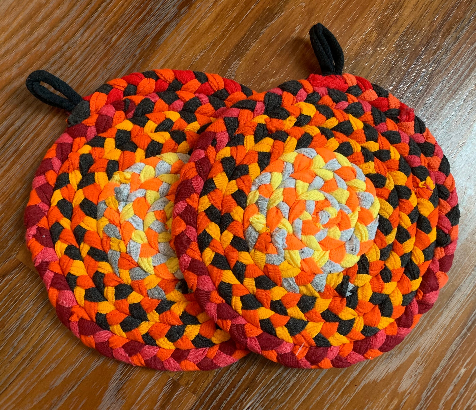 A set of two trivet potholders, side by side, lay flat on a wood surface.