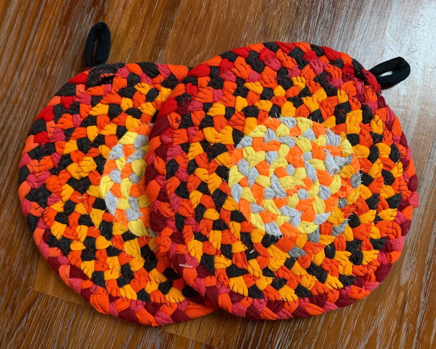 The back of two trivet potholders, to show off stitching, lay flat on a wood surface.