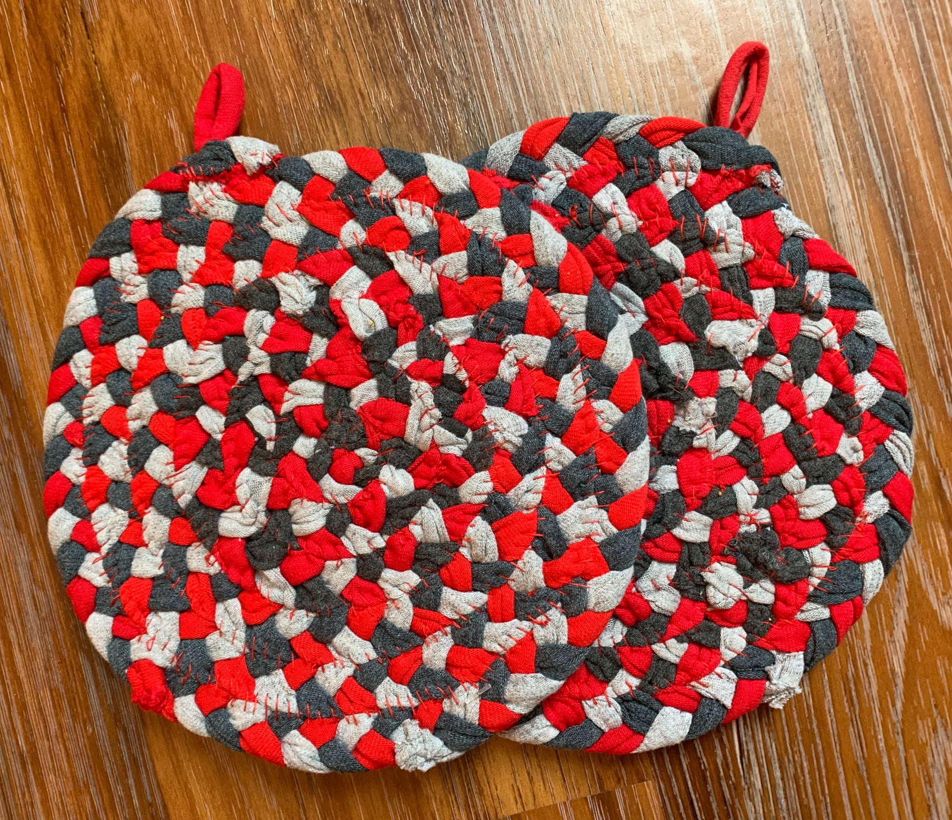 The back of two trivet potholders, to show off stitching, lay flat on a wood surface.