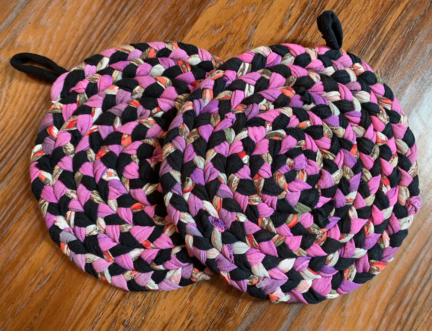 A set of two trivet potholders, side by side, lay flat on a wood surface.