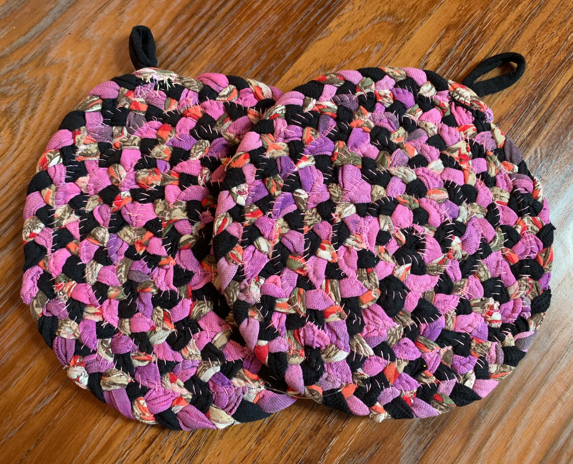 The back of two trivet potholders, to show off stitching, lay flat on a wood surface.