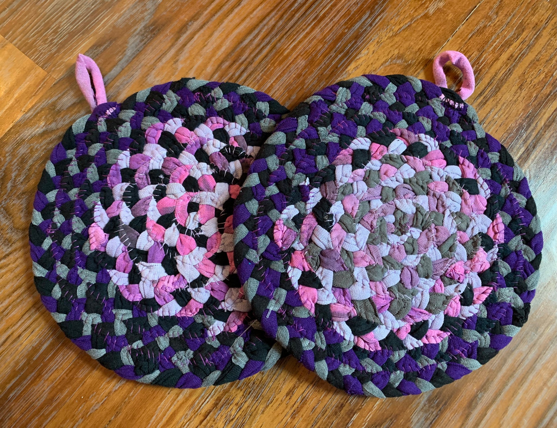 The back of two trivet potholders, to show off stitching, lay flat on a wood surface.