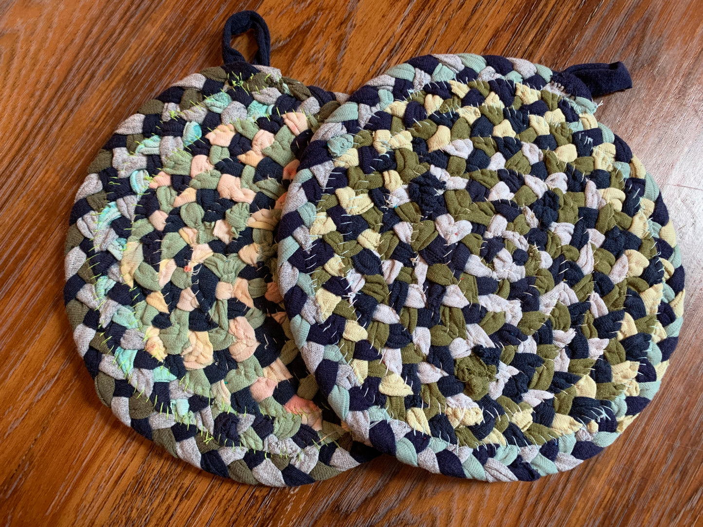 The back of two trivet potholders, to show off stitching, lay flat on a wood surface.