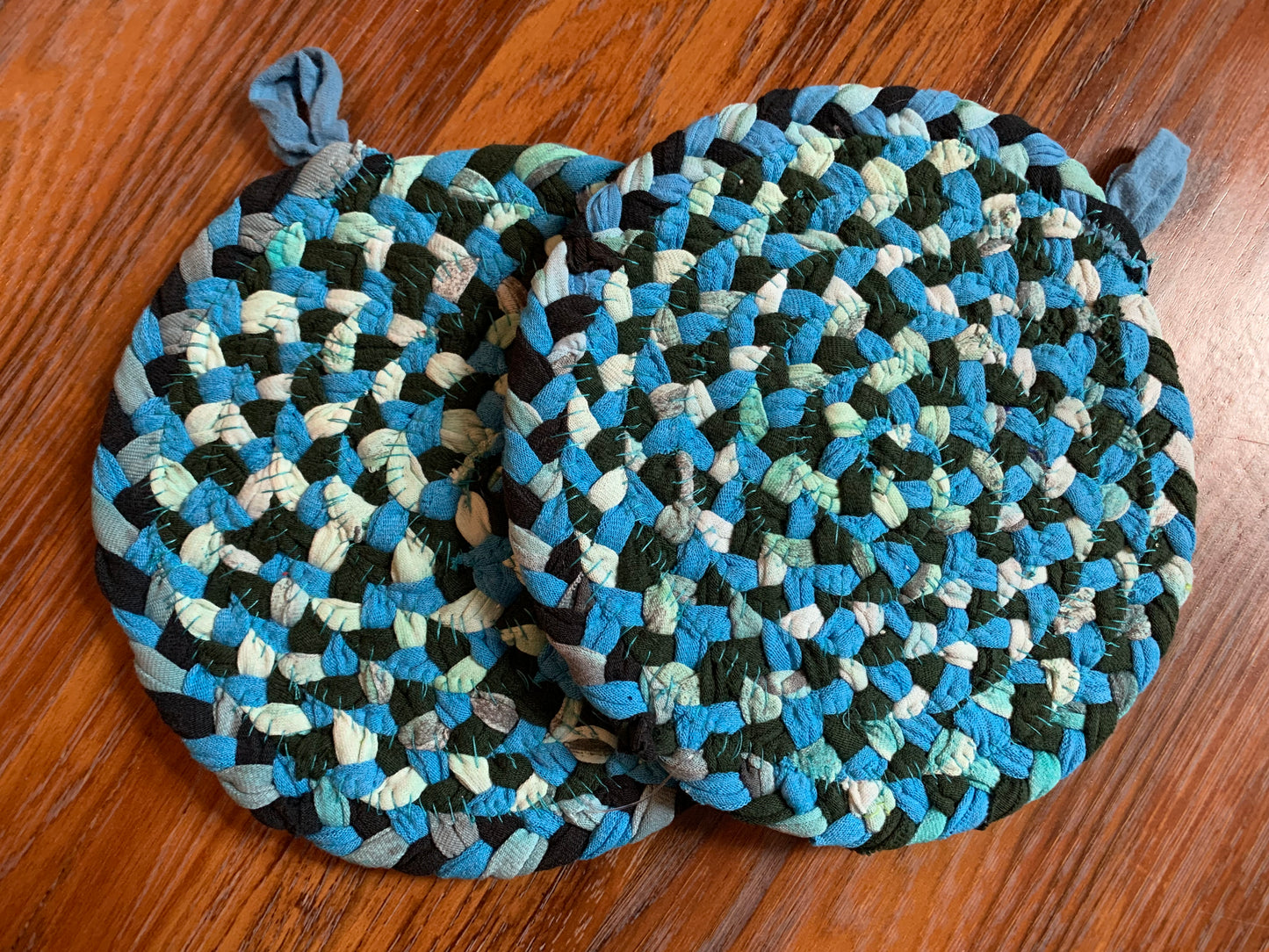 The back of two trivet potholders, to show off stitching, lay flat on a wood surface.