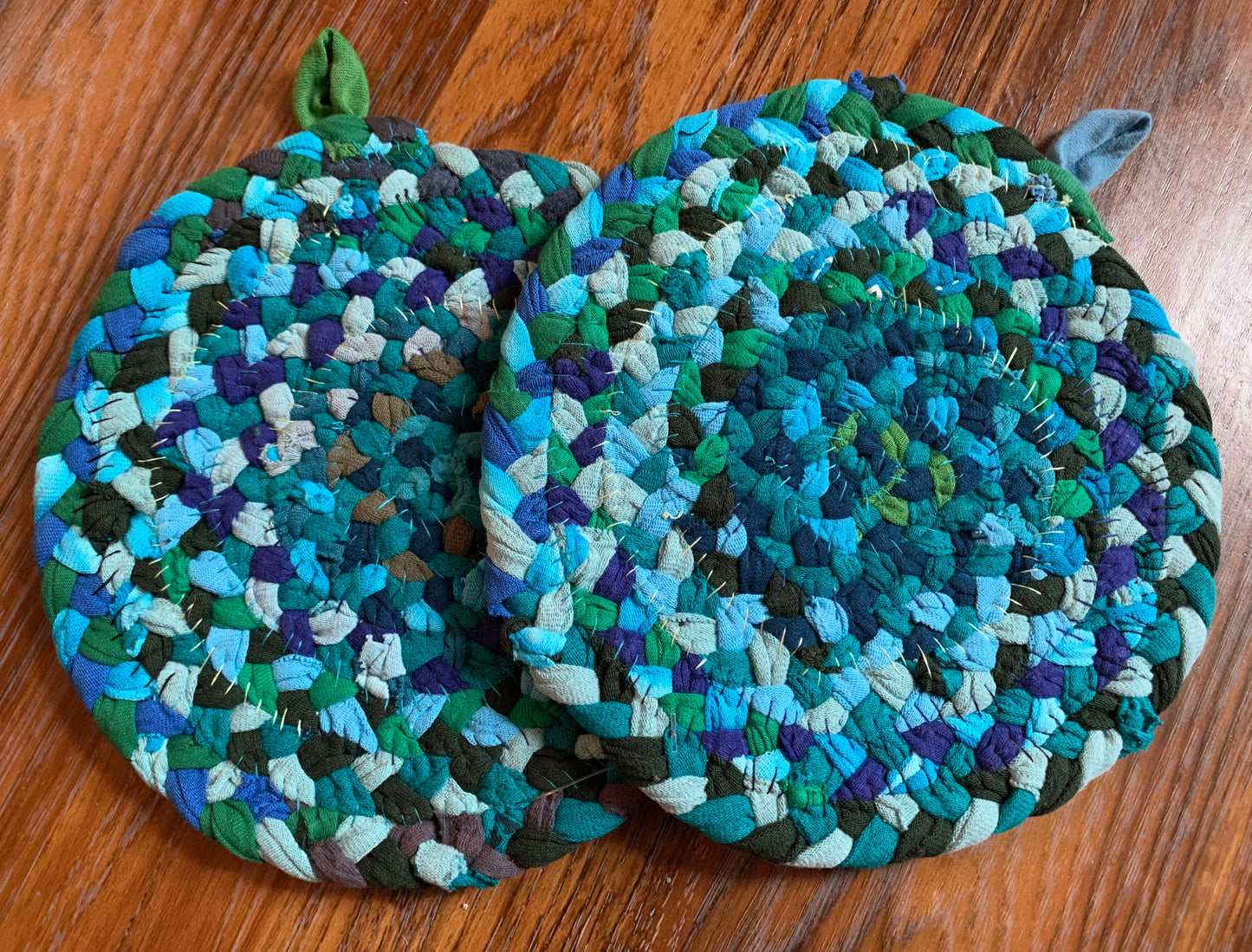 The back of two trivet potholders, to show off stitching, lay flat on a wood surface.