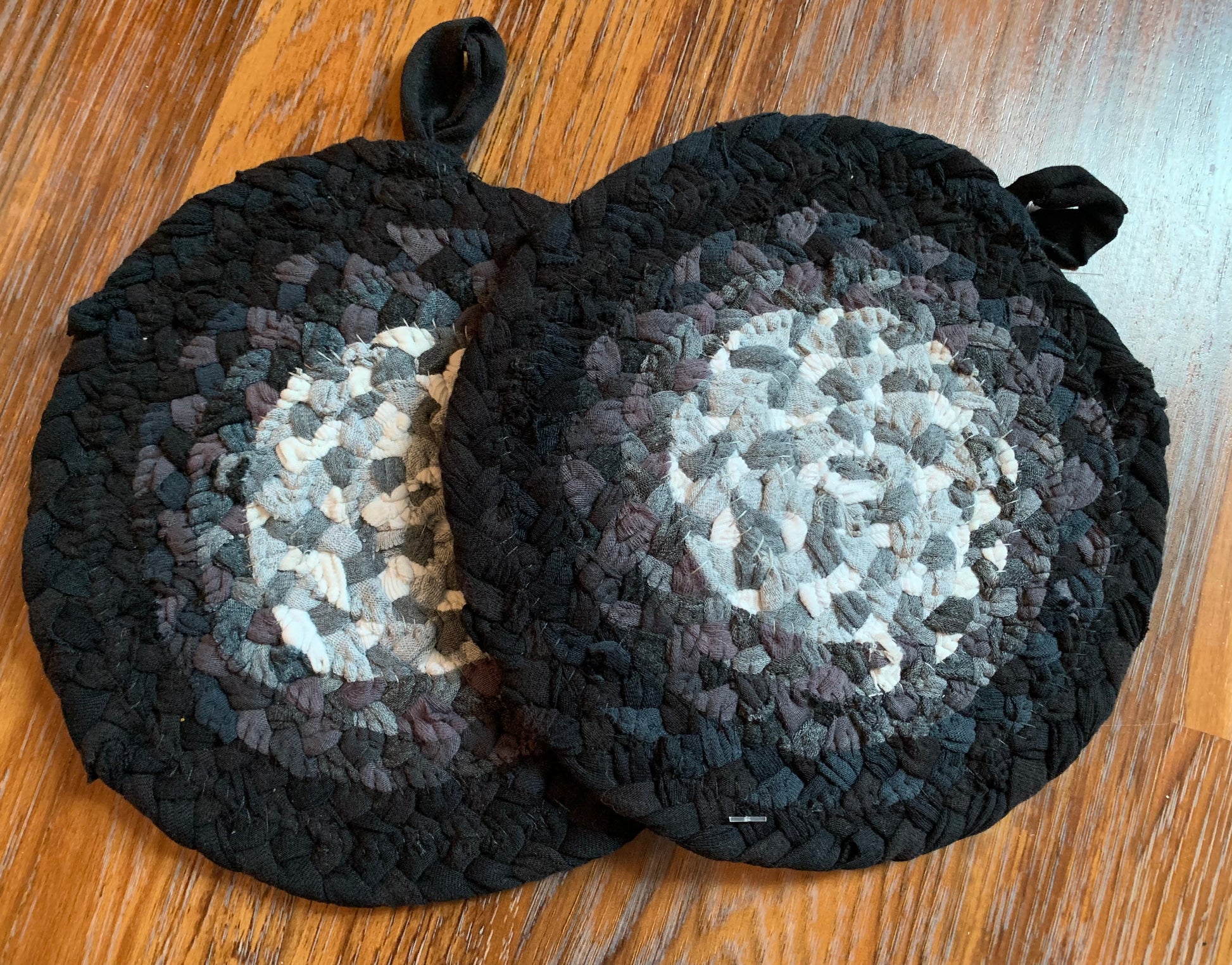 Back of a set of two trivet potholders, showing stitching, lay flat on a wood surface.