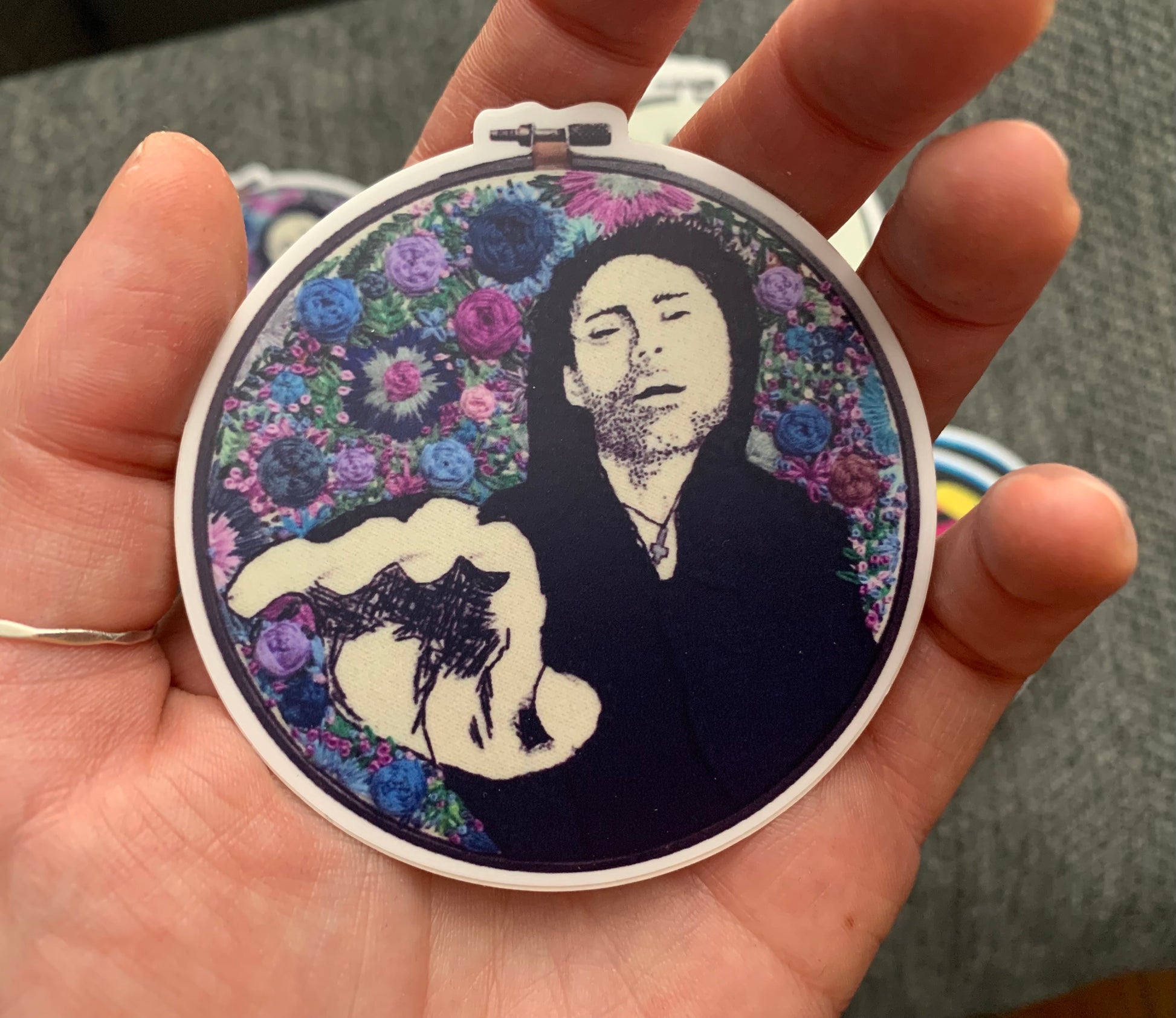 Davey Havok, reaching for the camera, in embroidery. with blue, purple flowers around him, embroidered. Embroidery hoop sticker design by me. AFI