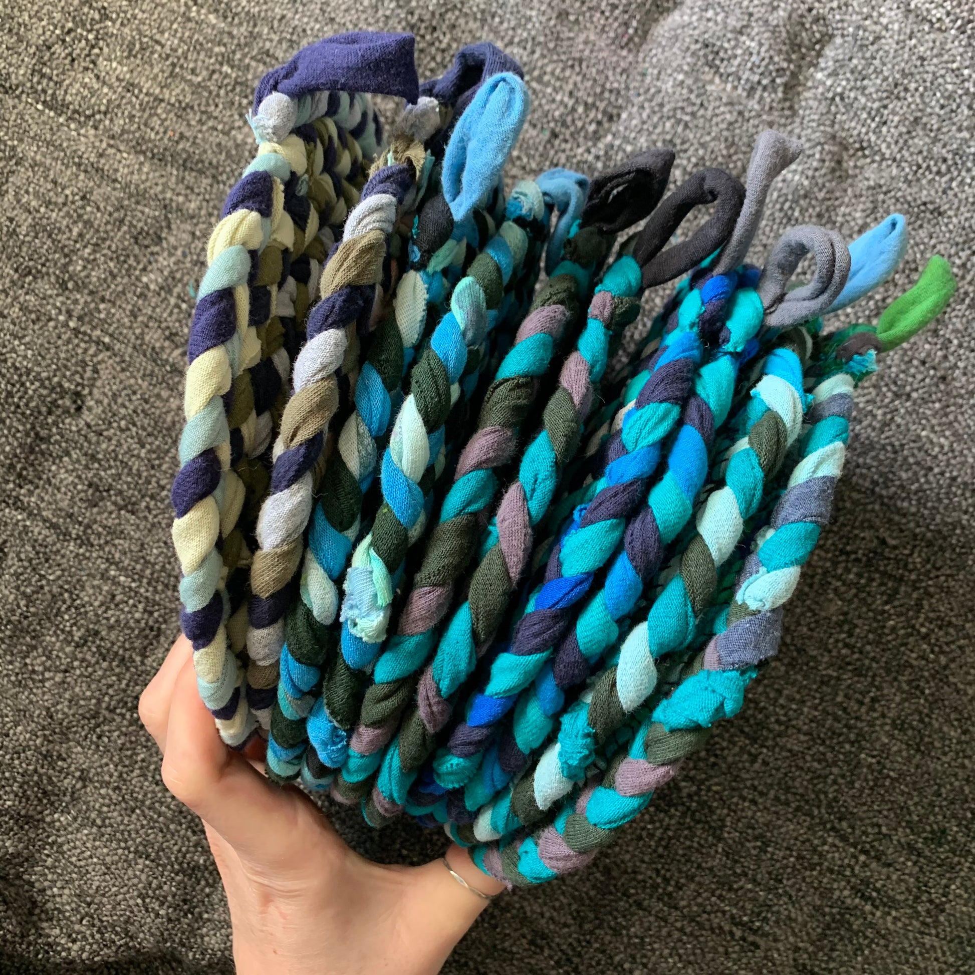 Group of green and blue trivet potholders, held by a hand, side view.