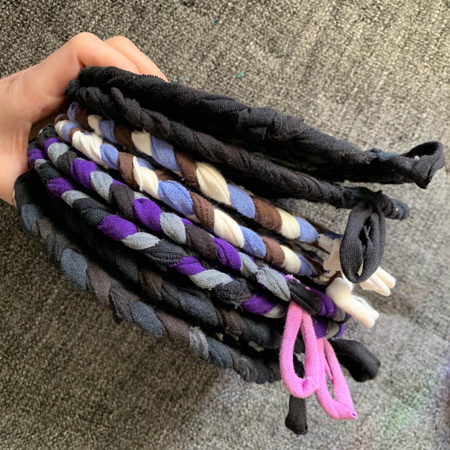 Group of blue purple and black trivet potholders, held by a hand, side view.