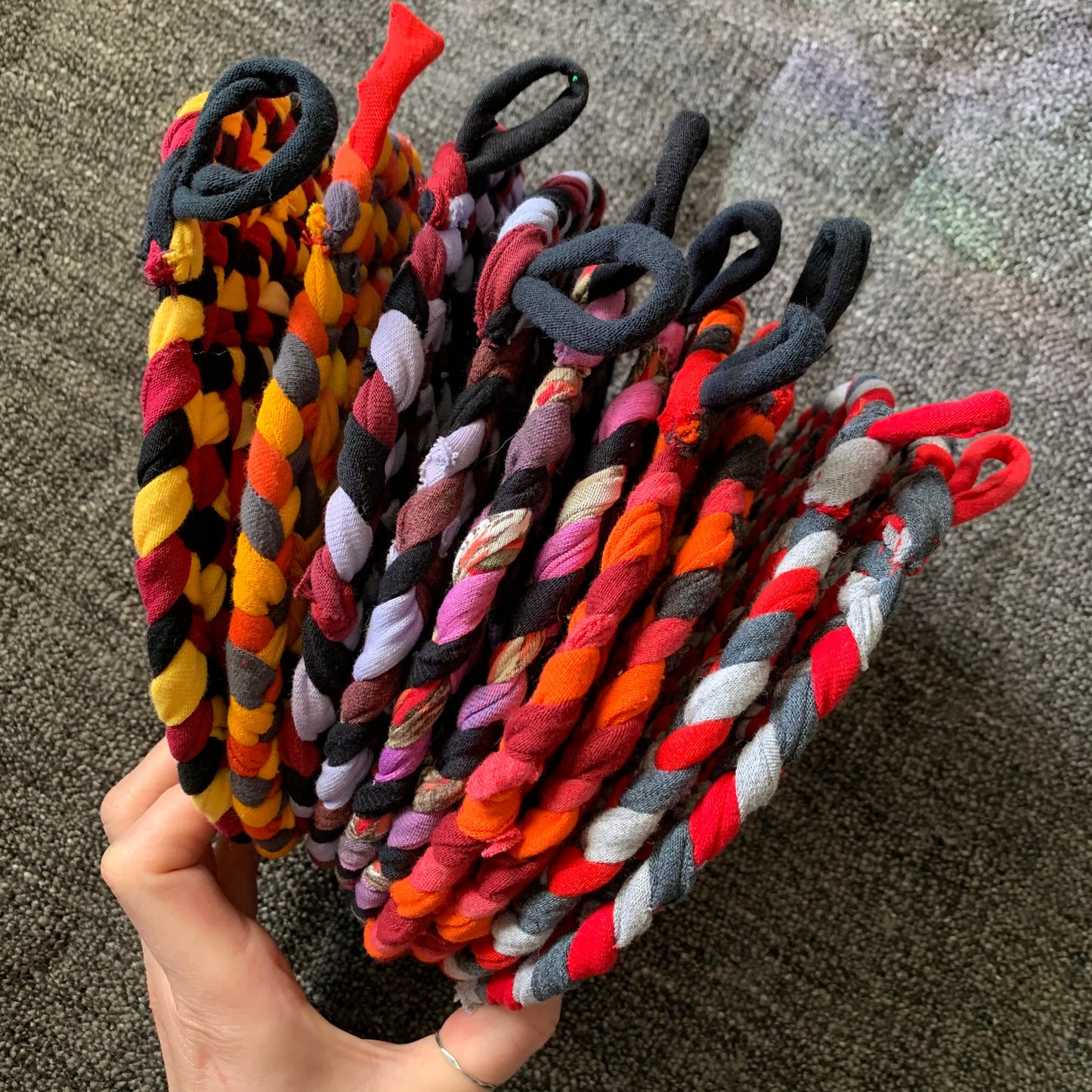 Group of red and orange trivet potholders, held by a hand, side view.