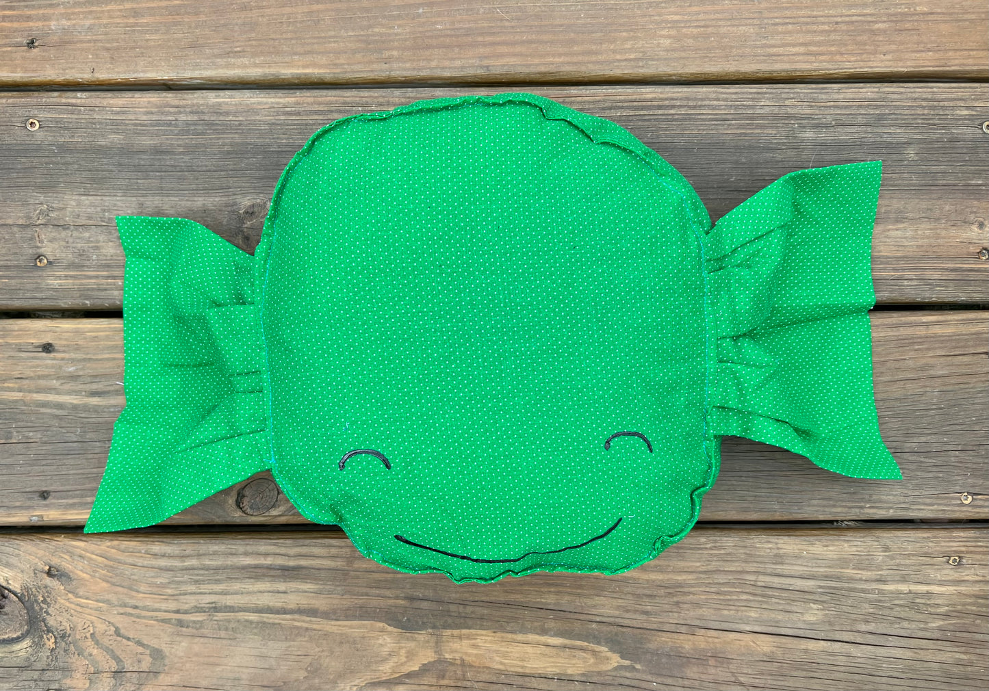 Green Apple candy pillow, against a wood background, with a painted face.