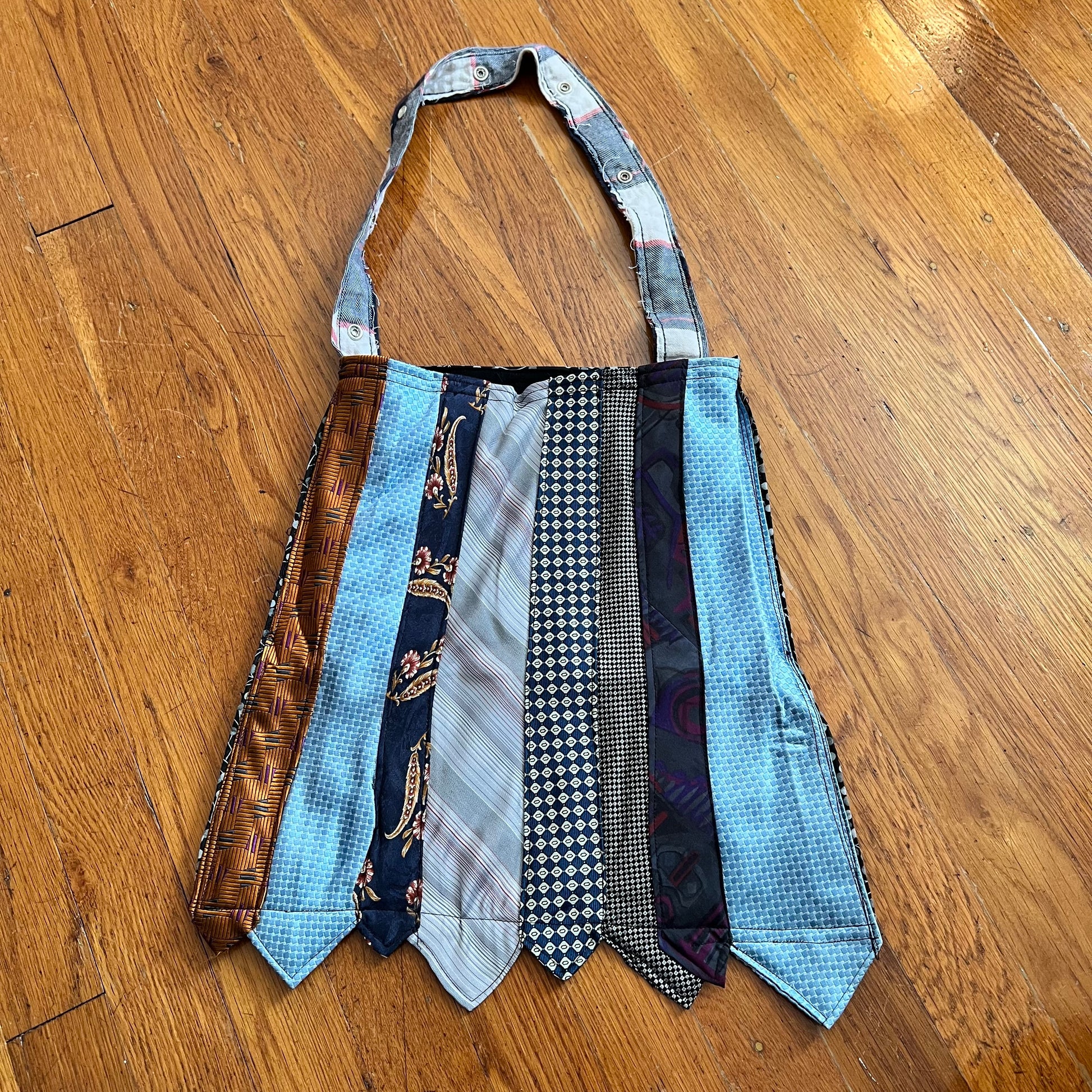 Tote bag created out of neckties in light blues, patterns, gold. wood floor background