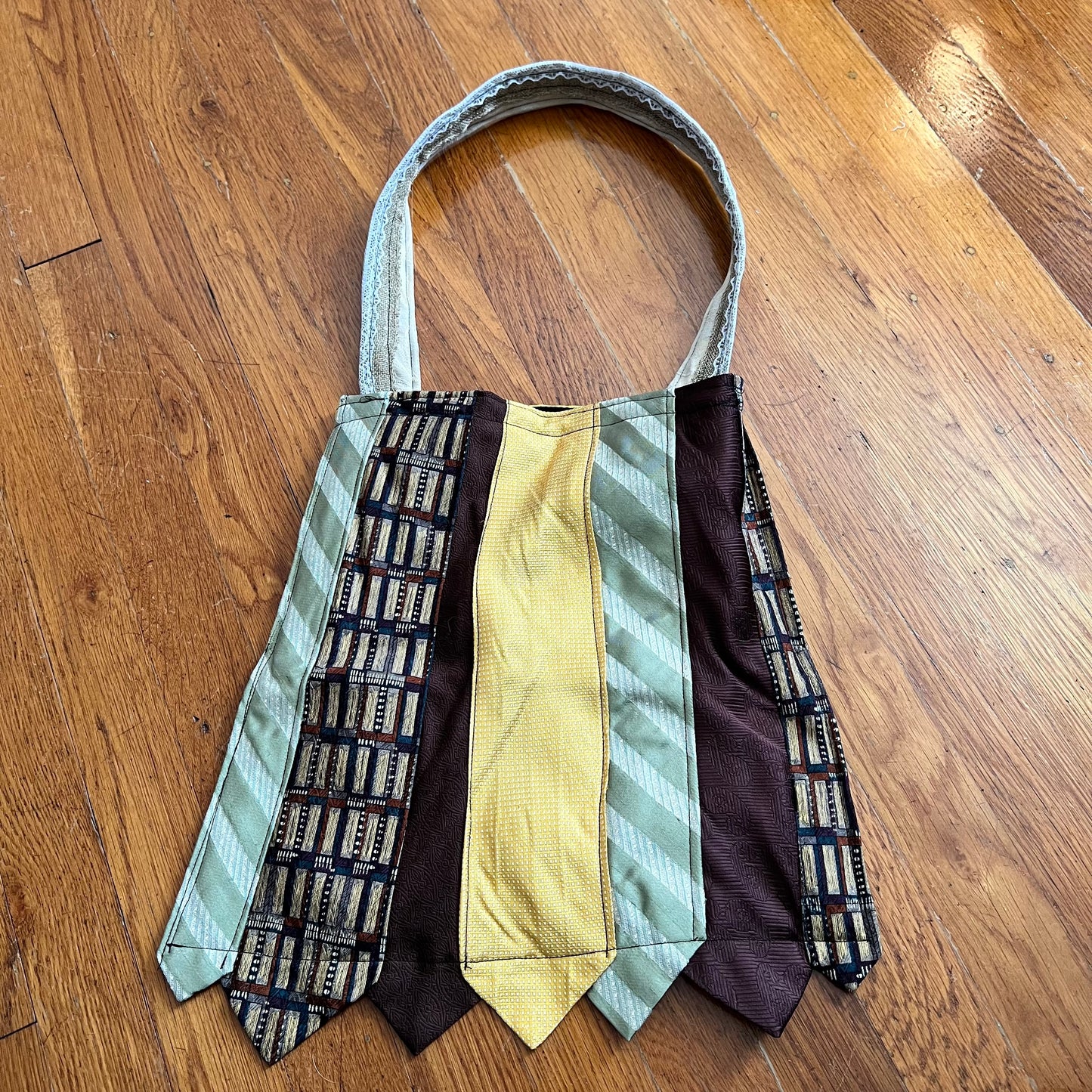Tote bag created out of neckties in sage green, yellow, brown. wood floor background