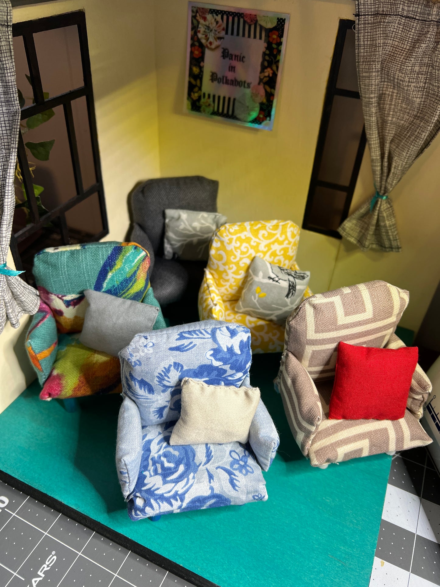 a collection of dollhouse chairs with pillows in a mini room setting, Panic in Polkadots sticker on wall.