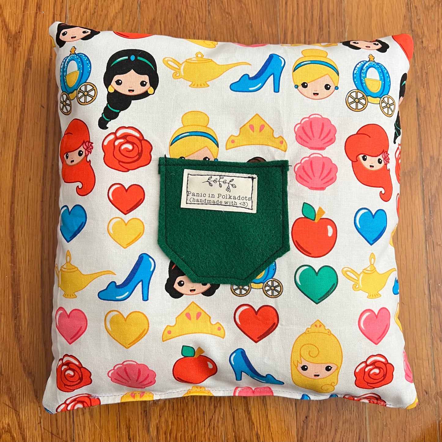 back view of pillow, with disney princess print, and a felt green pocket with Panic label