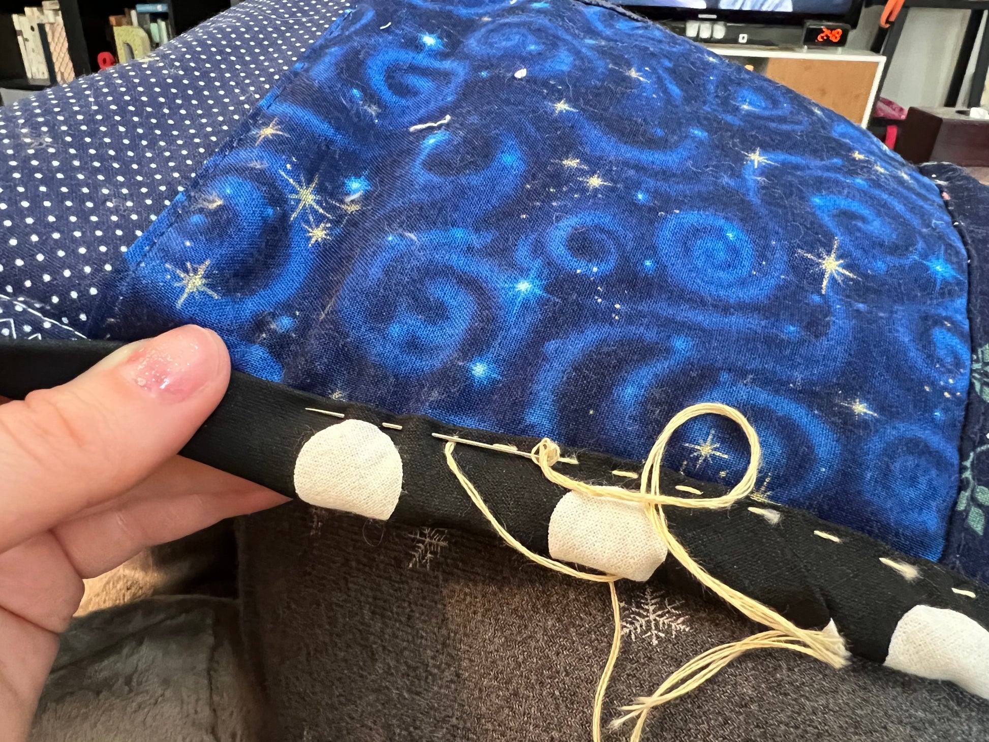 close up of hand stitched binding in progress.  hand holds the edge of the quilt, and a needle is pushed partially through