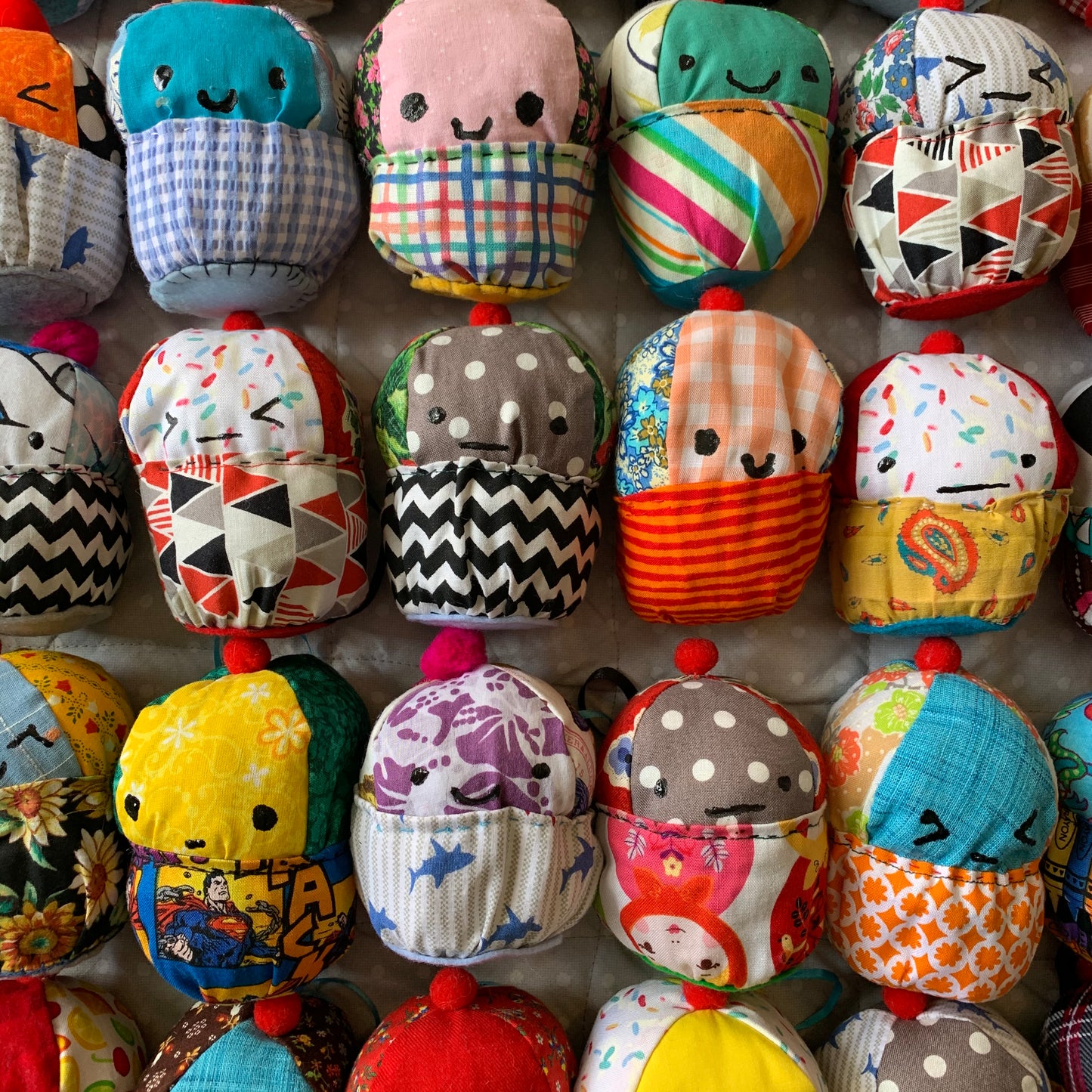 A closer view of colorful plush cupcakes with various facial expressions. Set up in a square formation.