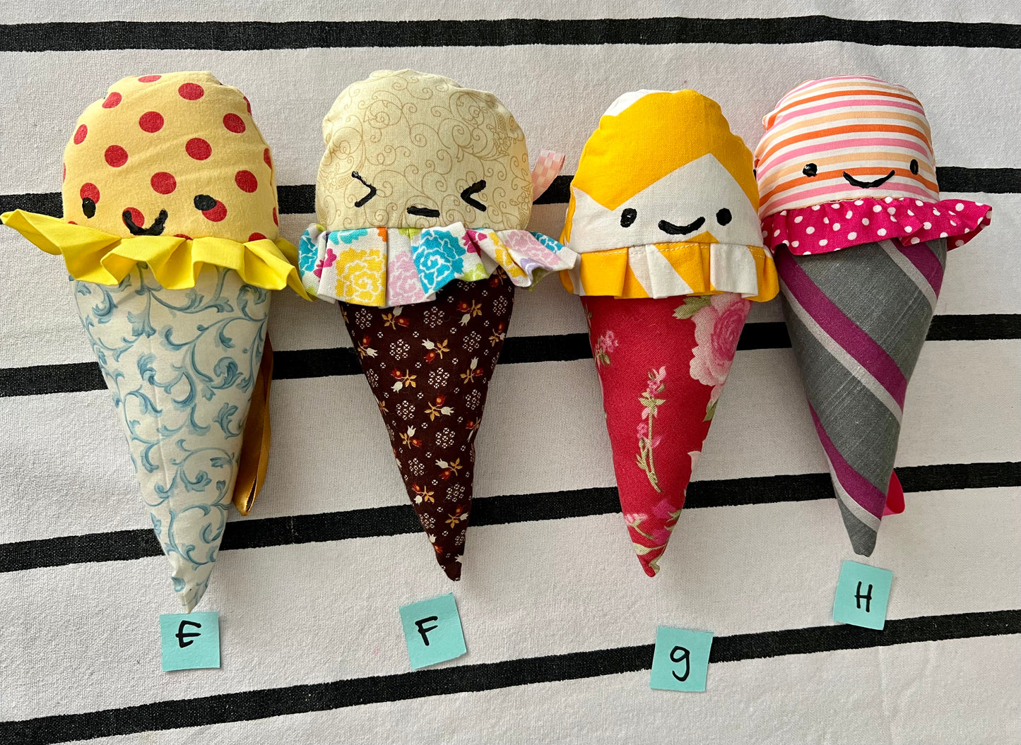 Ice cream cone plushies with handpainted faces, lined up with the letters E F G H below them