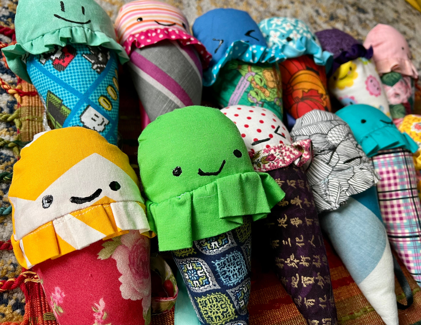 Collection of colorful fabric ice cream cone dolls with smiling faces on a textured surface