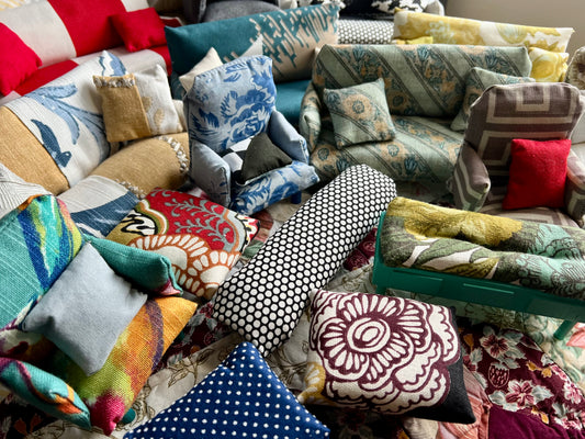Collection of colorful pillows on various miniature sofas and chairs, with different patterns and textures.
