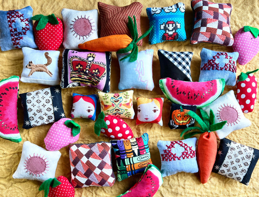 Collection of small decorative dollhouse pillows with various patterns and shapes on a yellow linen surface.